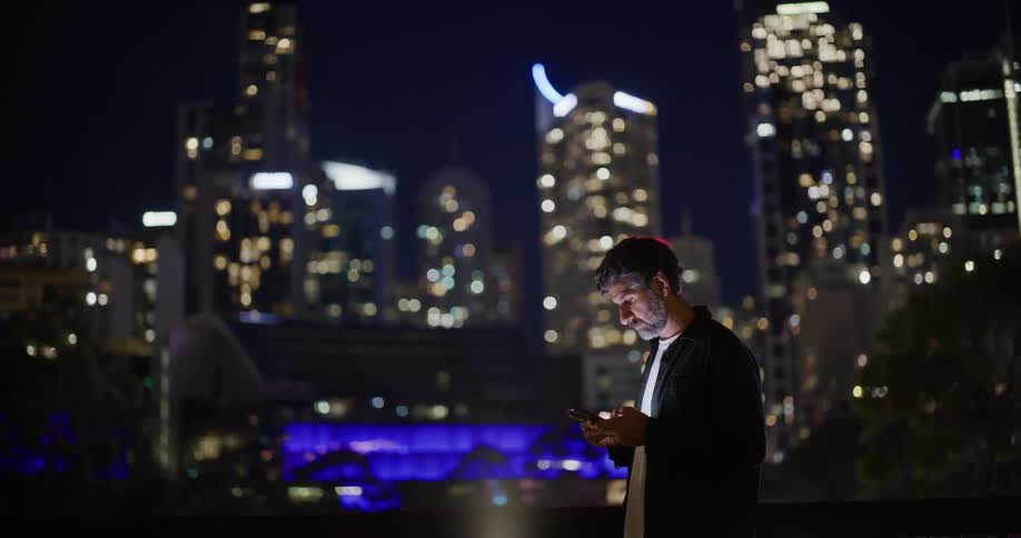 A male on his phone at night in a city near bright blue lights