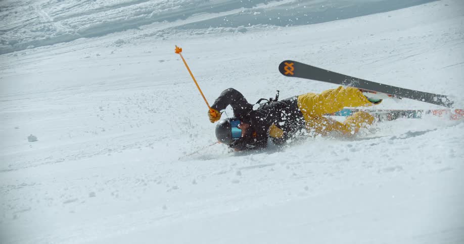 A skier in yellow pants and a black jacket loses their balance and falls on a snowy slope