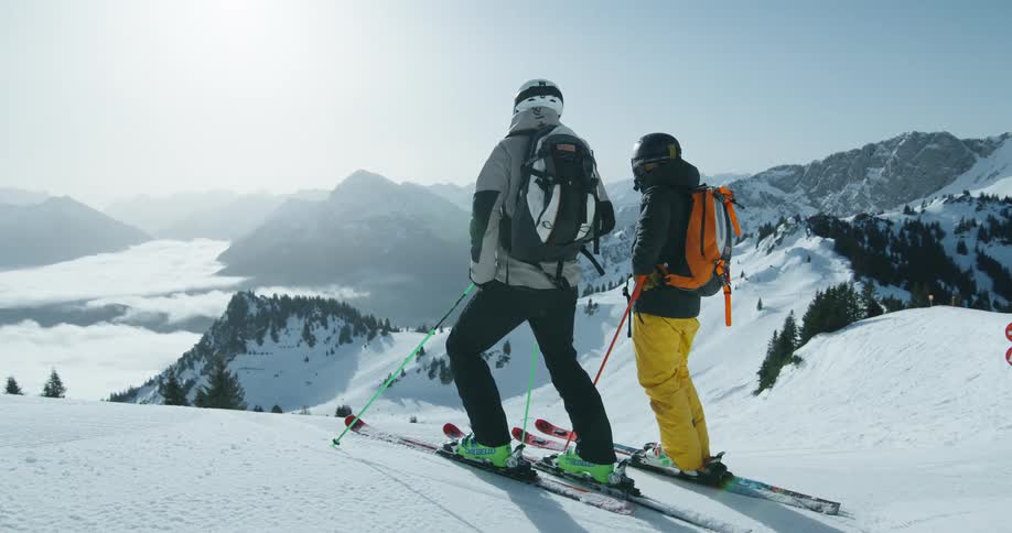 Two people with ski equipment on the peak of a snowy mountain