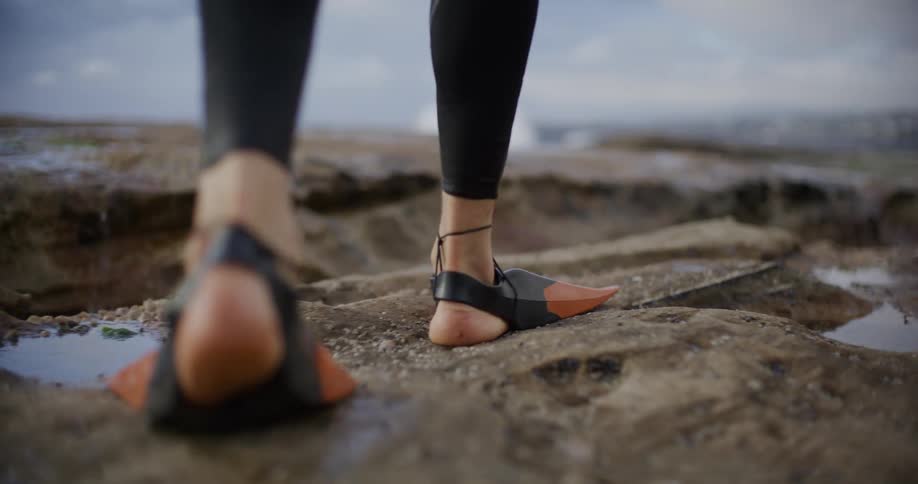 Legs of a person with flipper feet walking between rocks at the seashore