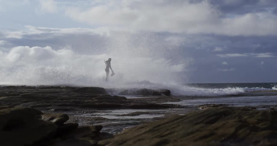A large wave hits a man standing on the shore line
