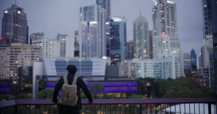 Man with a backpack walking and enjoying a panoramic view of skyscrapers in a metropolis at dusk