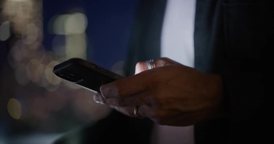 Bearded man standing outdoors using a mobile phone on an urban area during night time
