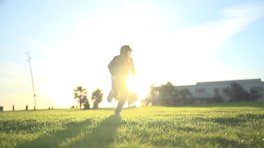 Young boy running across a grassy field at sunset