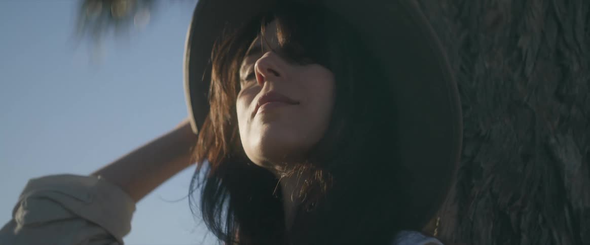 Woman in hat leaning against a tree