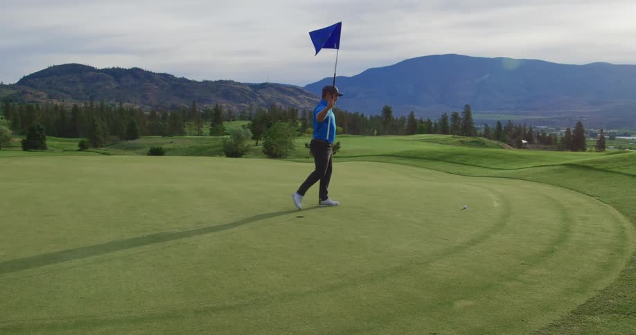 A man carries a blue flag on a large golf course near a hole