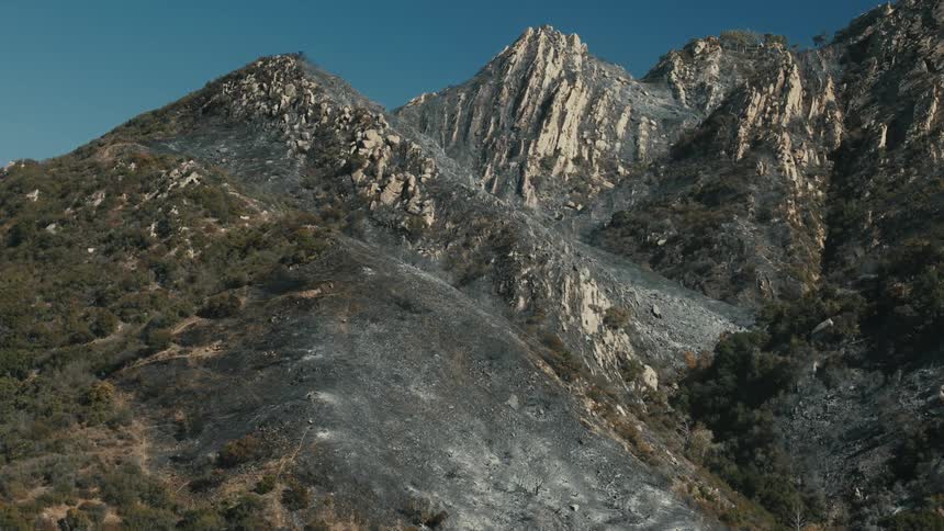 A mountainous landscape with a contrast between the dark firescarred slopes and green foliage