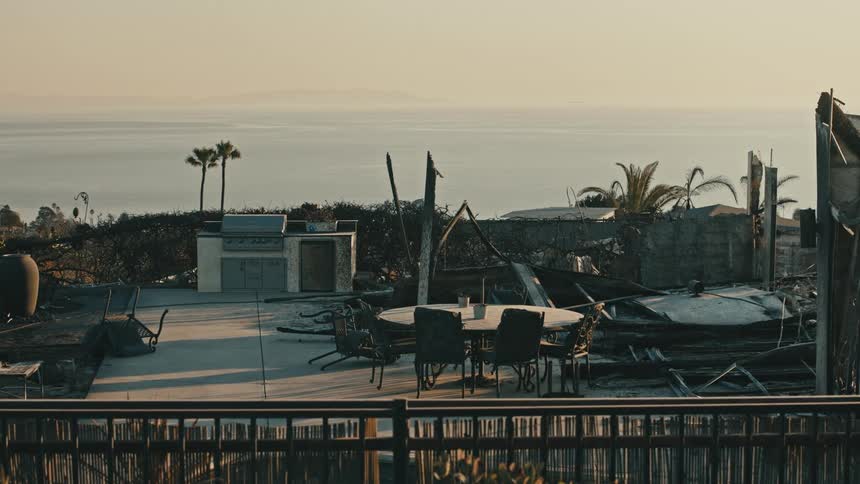 A partially destroyed outdoor patio area with a table and chairs overlooking an ocean with palm trees
