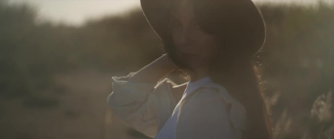 A young woman wearing a cap has her back turned and then turns around