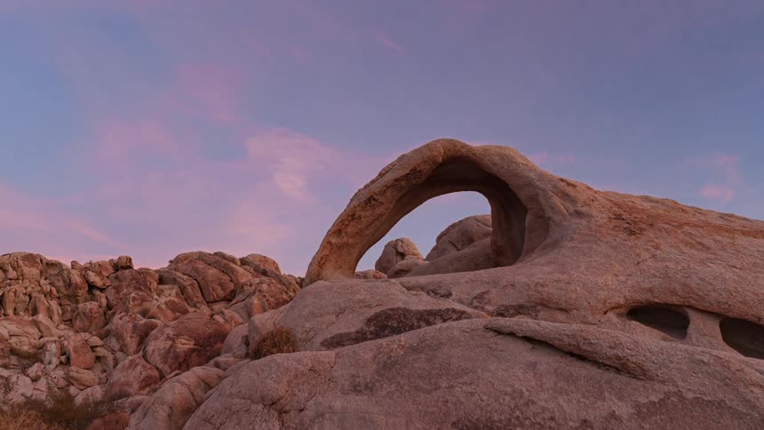 A rock formation with a natural arch stands against a backdrop of a twilight sky which is a mix of blue and pink