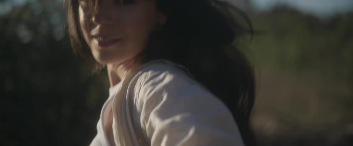 A female wearing a crop top and jeans is smiling and walking in a field