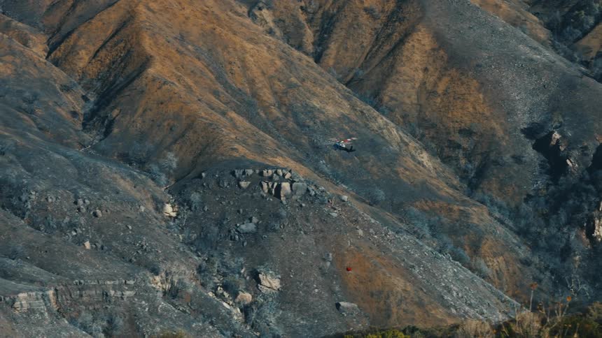 Helicopter flies over arid burned slopes