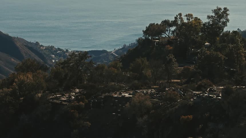 The remnants of buildings on a hilltop surrounded by a coastal landscape with views of the ocean and forested areas in the background