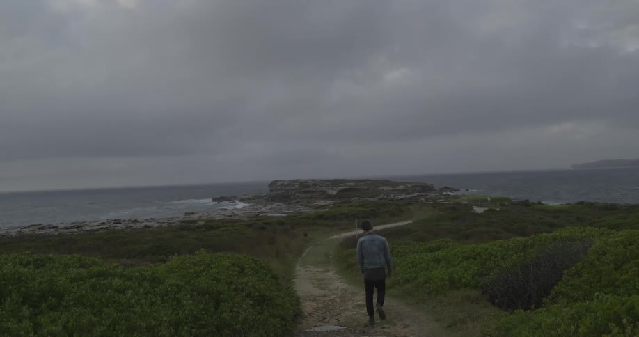 Man walking down a path to the shore on a cloudy day