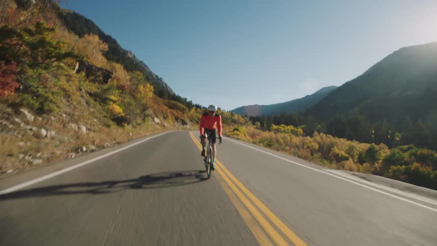 Cyclist rides his bicycle along a highway passing forested hills and mountains on a sunny autumn day