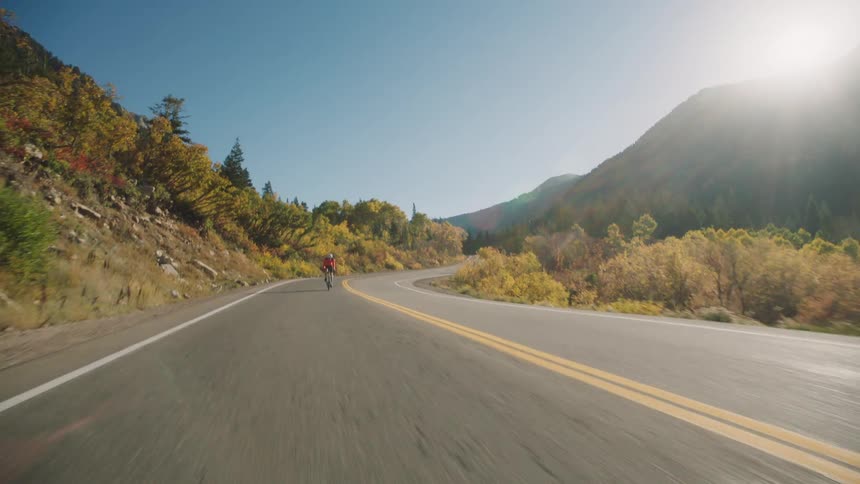 Cyclist rides his bicycle along a highway passing forested slopes during a sunny autumn day
