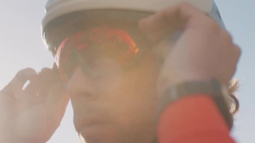 A person wearing a helmet puts on reflective sunglasses with the reflection showing a cyclist