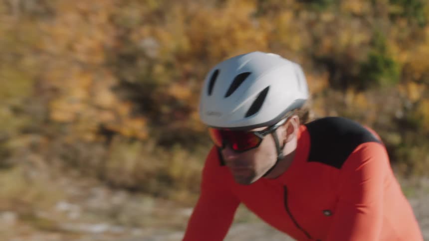 Leaves are changing on the trees lining a road where a cyclist pedals