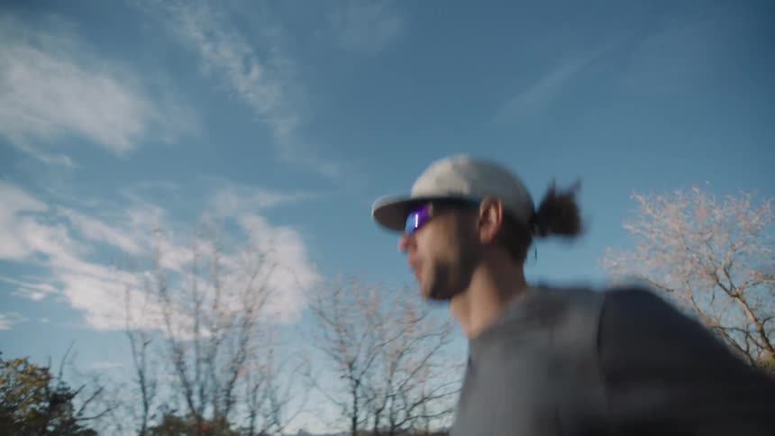 A man jogs down the street next to an empty field near some woods