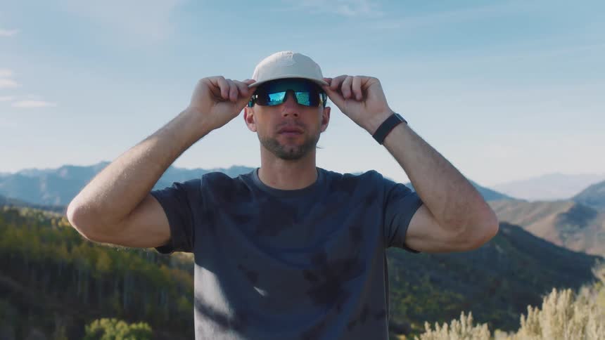 A man standing in the mountains adjusts his sunglasses