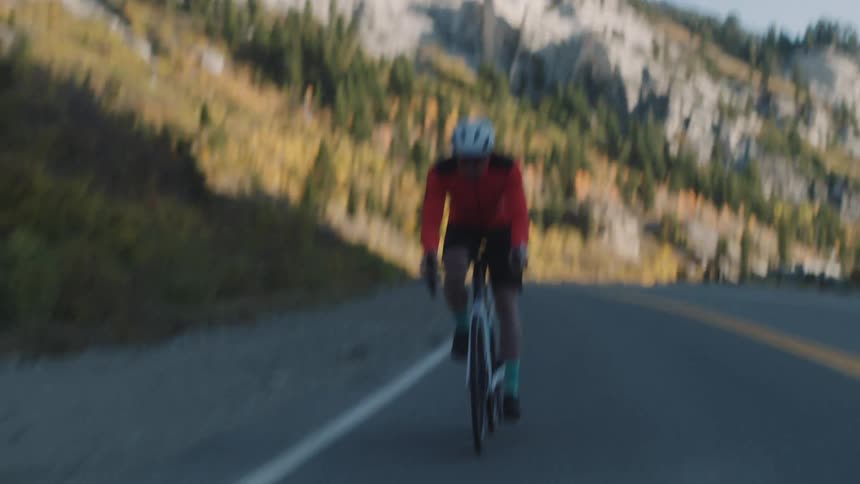 A cyclist wearing a red jacket and white helmet is riding a bicycle on a winding mountain road