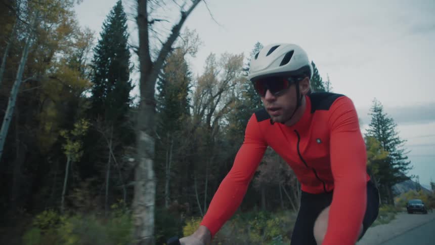 A man is cycling on a forested highway on a cloudy autumn day