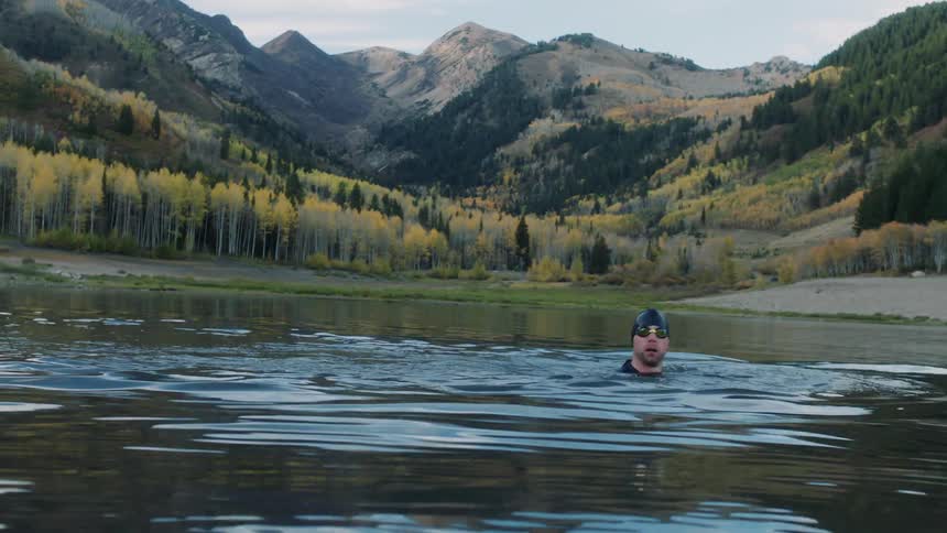 Man in swimming cap swimming in a lake surrounded by mountains