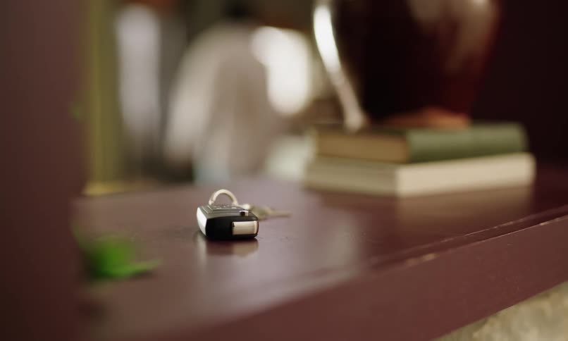 Person placing a car key on top of a bookshelf