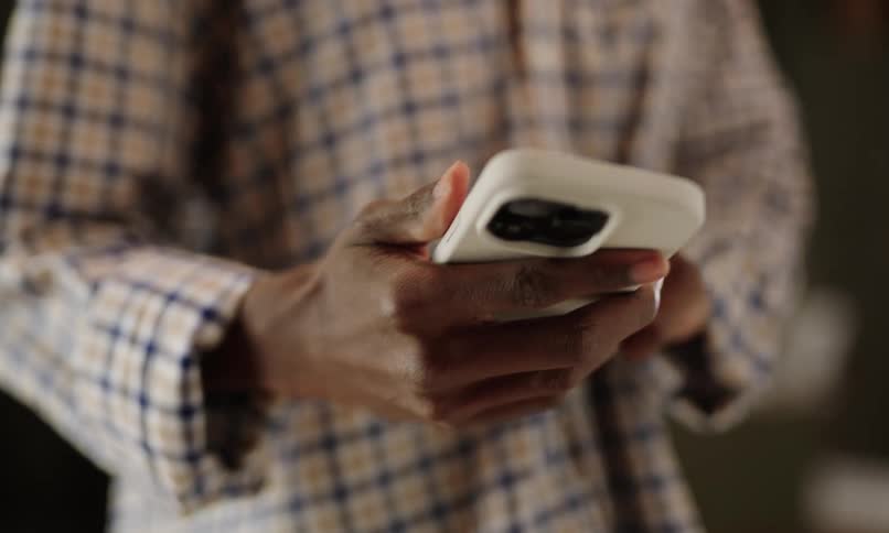 A person wearing a plaid shirt answers a call on a white smartphone