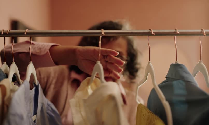 A clip of an elderly female browsing through some clothes on the hanger