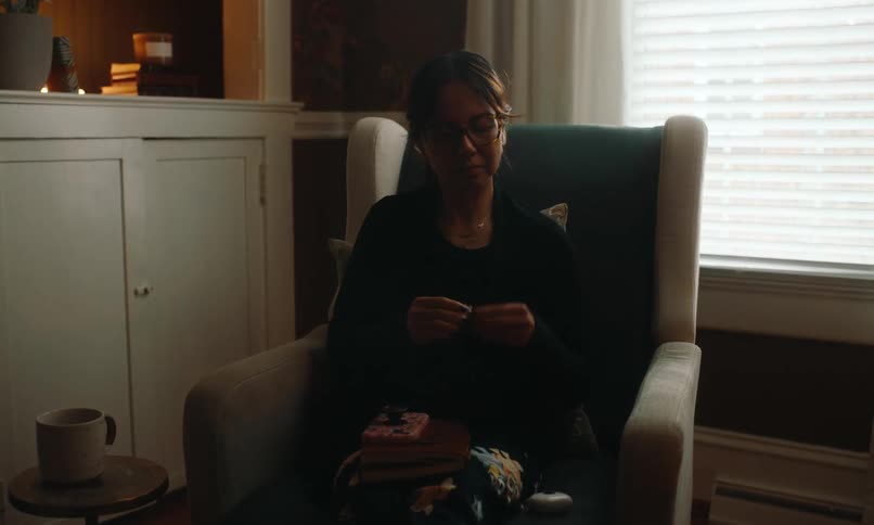 Woman sitting in an armchair drinking from a mug and putting on headphones