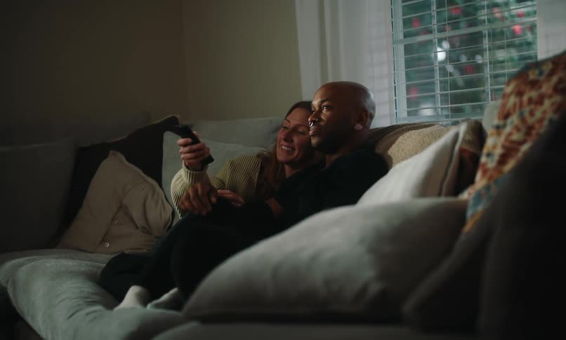 Couple sitting together on sofa with woman using television remote control
