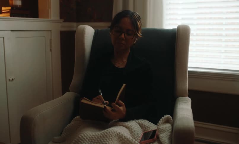 A clip of a lady seating on a chair and writing in a book