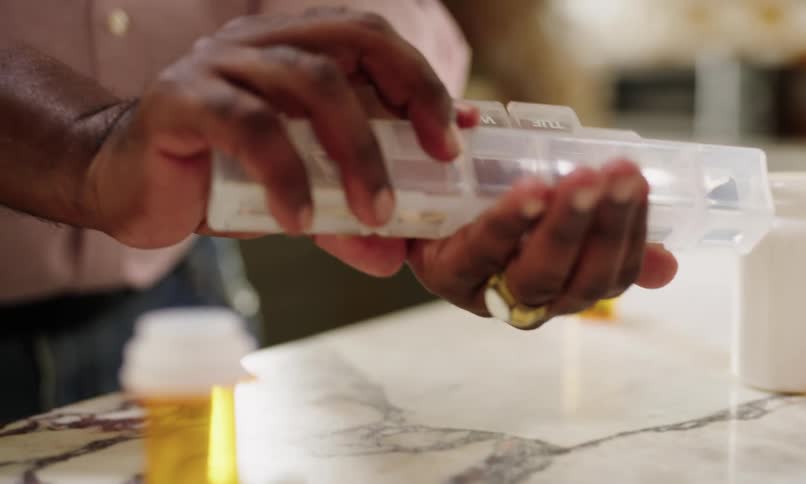 A person is taking their daily medication from a weekly pill organizer