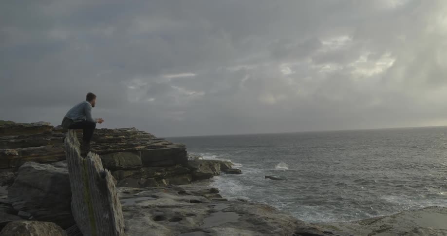 A man sits on a rock near the ocean