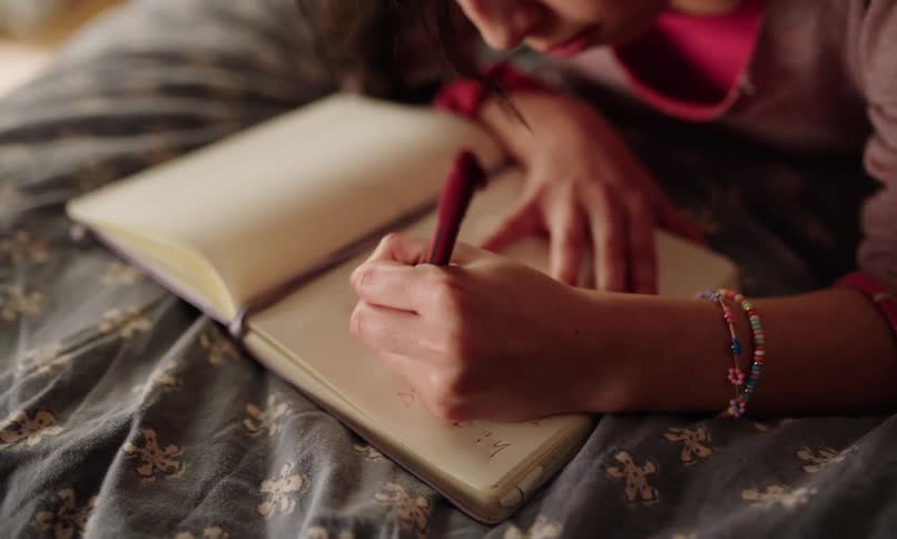 A young left-handed girl focused on writing in an open notebook with a pen