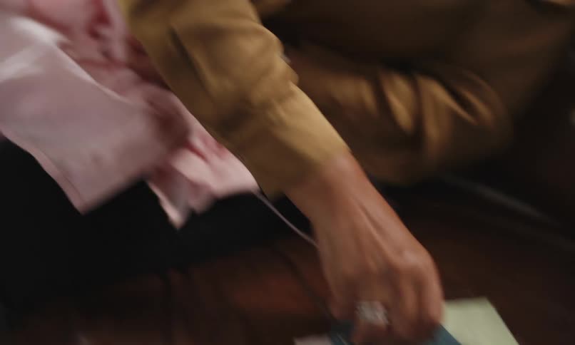 A person in yellow clothes is sewing a pink fabric and cutting the thread with scissors