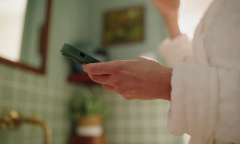 Close up of a persons hand typing on a smartphone while brushing their teeth with the other hand