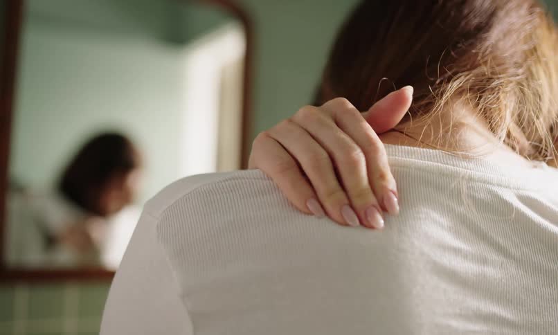 Woman massaging her back in front of a mirror