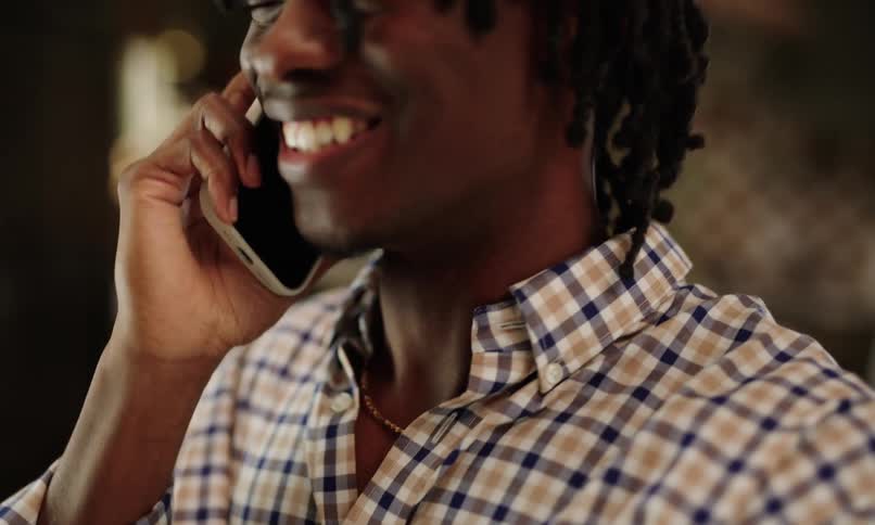 A person wearing a checkered shirt is holding a smartphone to the ear engaged in a phone call