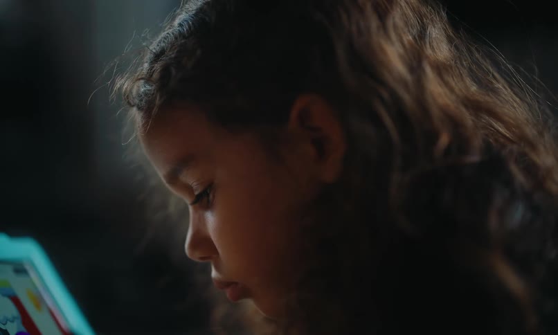 A girl with curly hair looks down at a screen