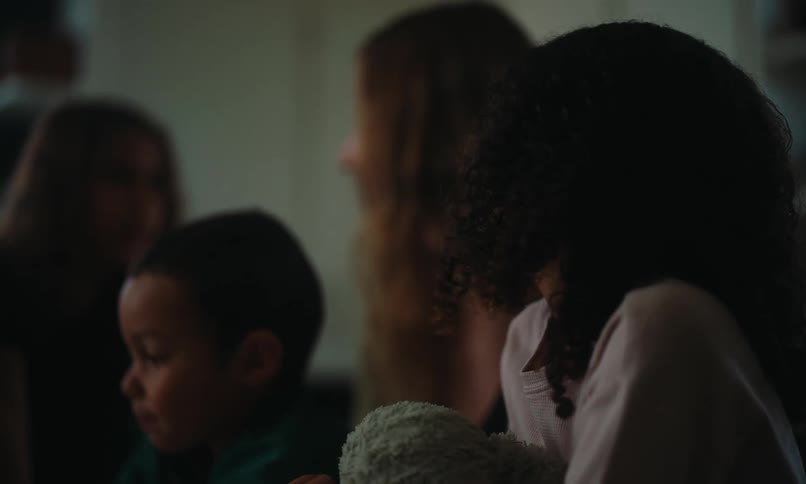 A father and mother along with their three children are gathered around a table inside a home looking at something out of view