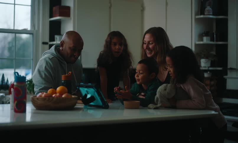 A family gathers around a kitchen counter sharing a moment together while looking at a tablet creating a warm and cozy atmosphere