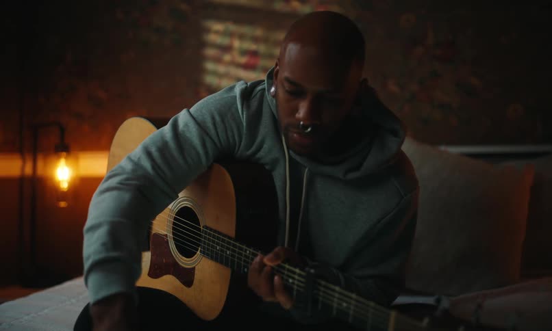 Man with a nose piercing and a light blue hoodie plays a guitar