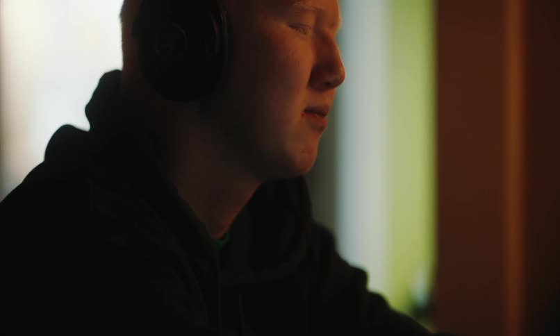 A person with fair skin and headphones is using a tablet in a dimly lit room