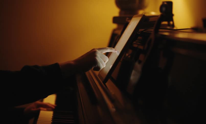 Man sitting playing piano and interacting with a tablet in front of him
