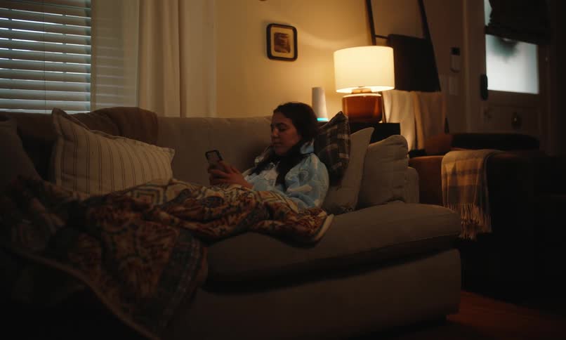 Woman lying on the living room sofa with a blanket and typing on a smartphone
