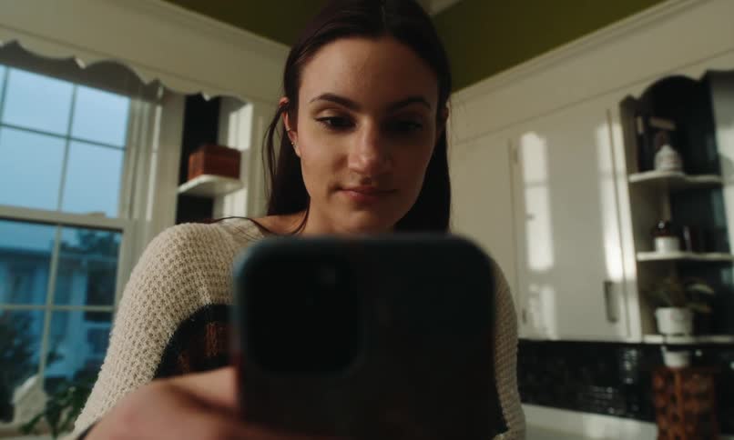 A woman lifts her phone in the kitchen and begins typing
