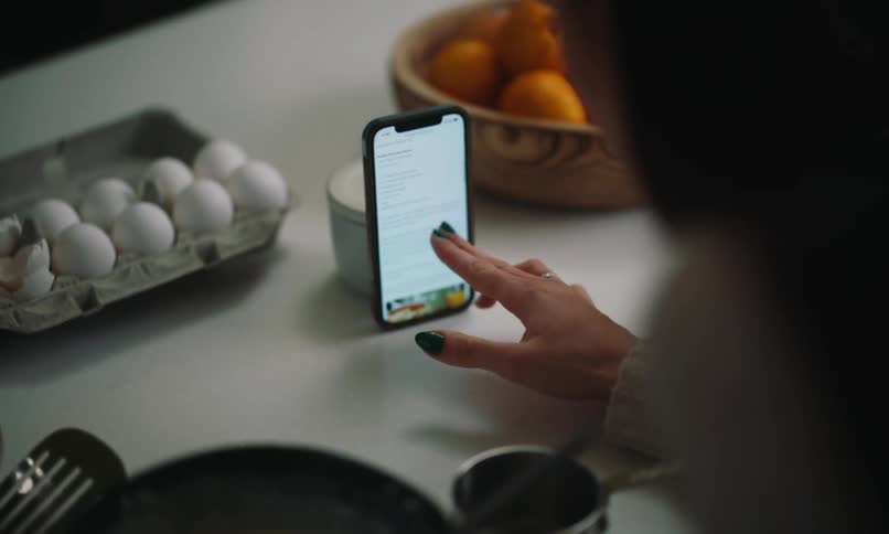 A person stirring a utensil in a pan of yellow food and then moving a cell phone with the screen on