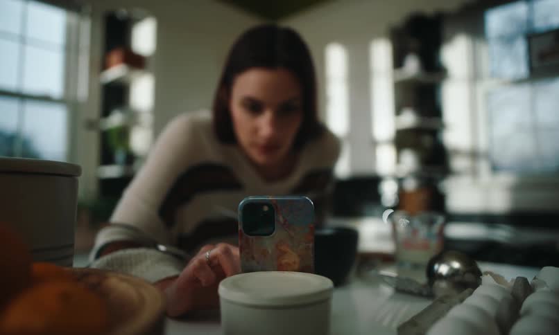 A woman looks at a recipe on her phone and uses a whisk